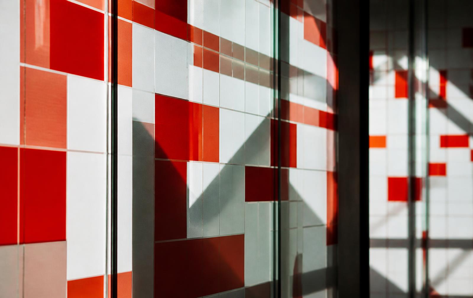 Modular red, white and grey grid panels behind architectural glass, casting geometric shadows